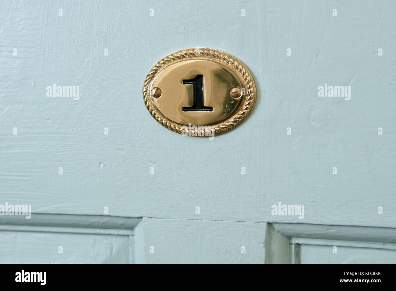 A black number one on a brass plaque, affixed to the front door of a UK home indicating it's address. Stock Photo