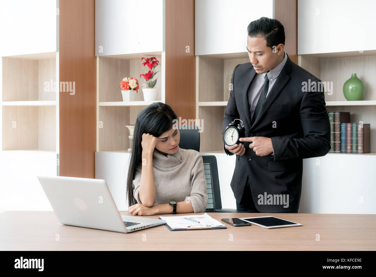 Angry business manager pointing his watch to subordinate businesswoman working missed deadline. Boss and worker at work having conflict. Stock Photo