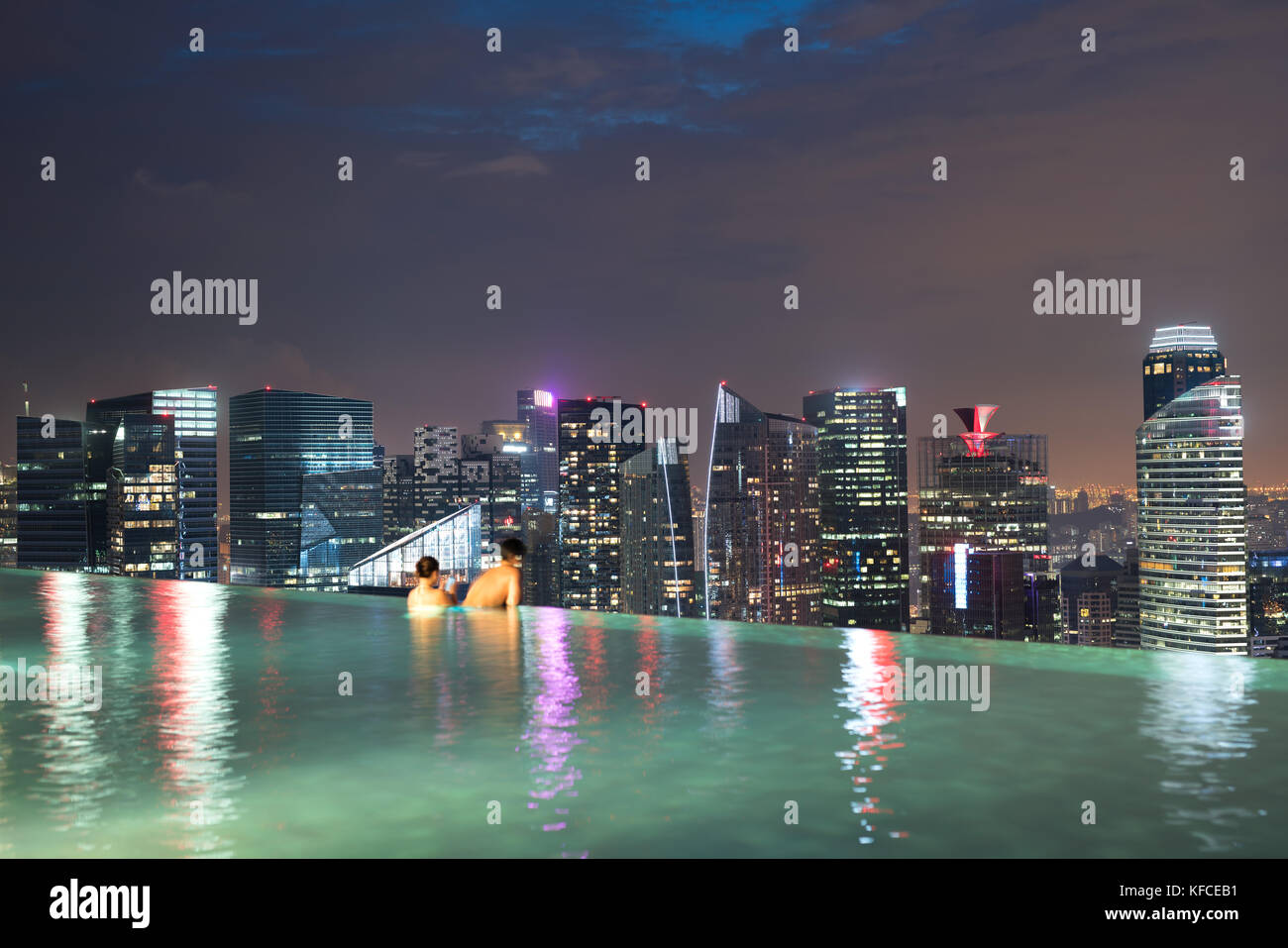 Asian couple swimming in the hotel roof top swimming pool taking in the Singapore city sights in the evening in Singapore. Stock Photo