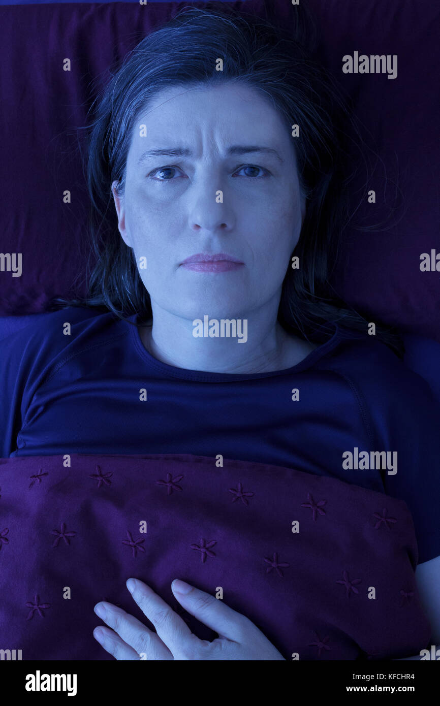 Middle aged woman lying awake in her bed at night, worrying because of an uncomfortable pressure in her chest and an irregular heartbeat Stock Photo