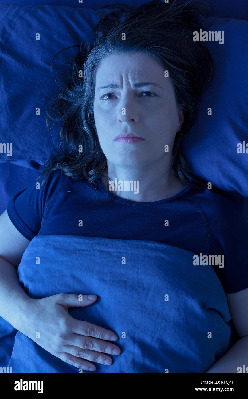 Middle aged woman lying awake in her bed at night because of insomnia, stress, fears, nightmares or restless leg syndrome Stock Photo