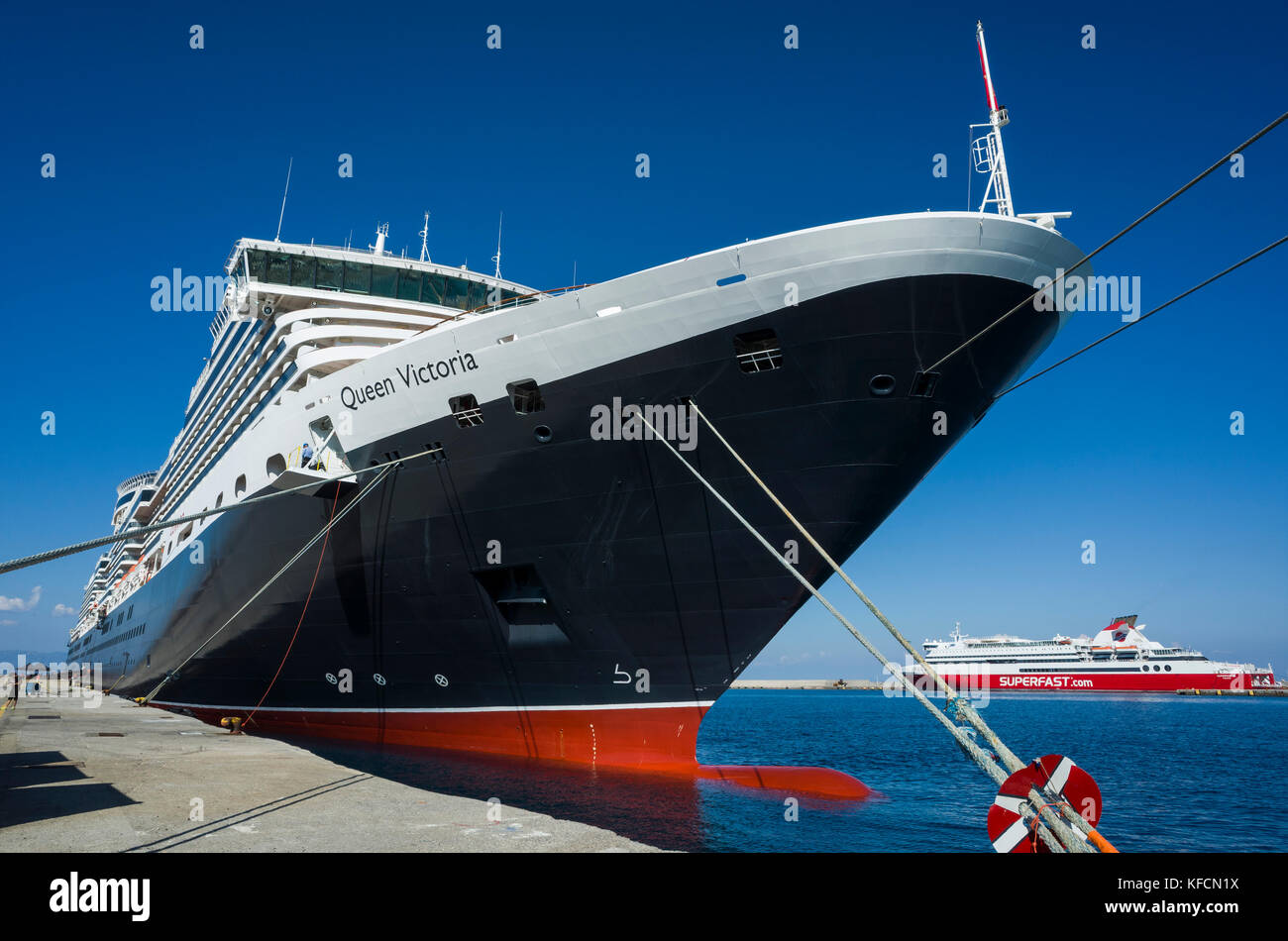 Rhodes Tourist Harbour, Rhodes. Crete.  Greece.  Cunard's luxury cruise liner, Queen Victoria, moored on the quayside.  It's a sunny day with a pure blue sky reflecting in the ocean. Stock Photo