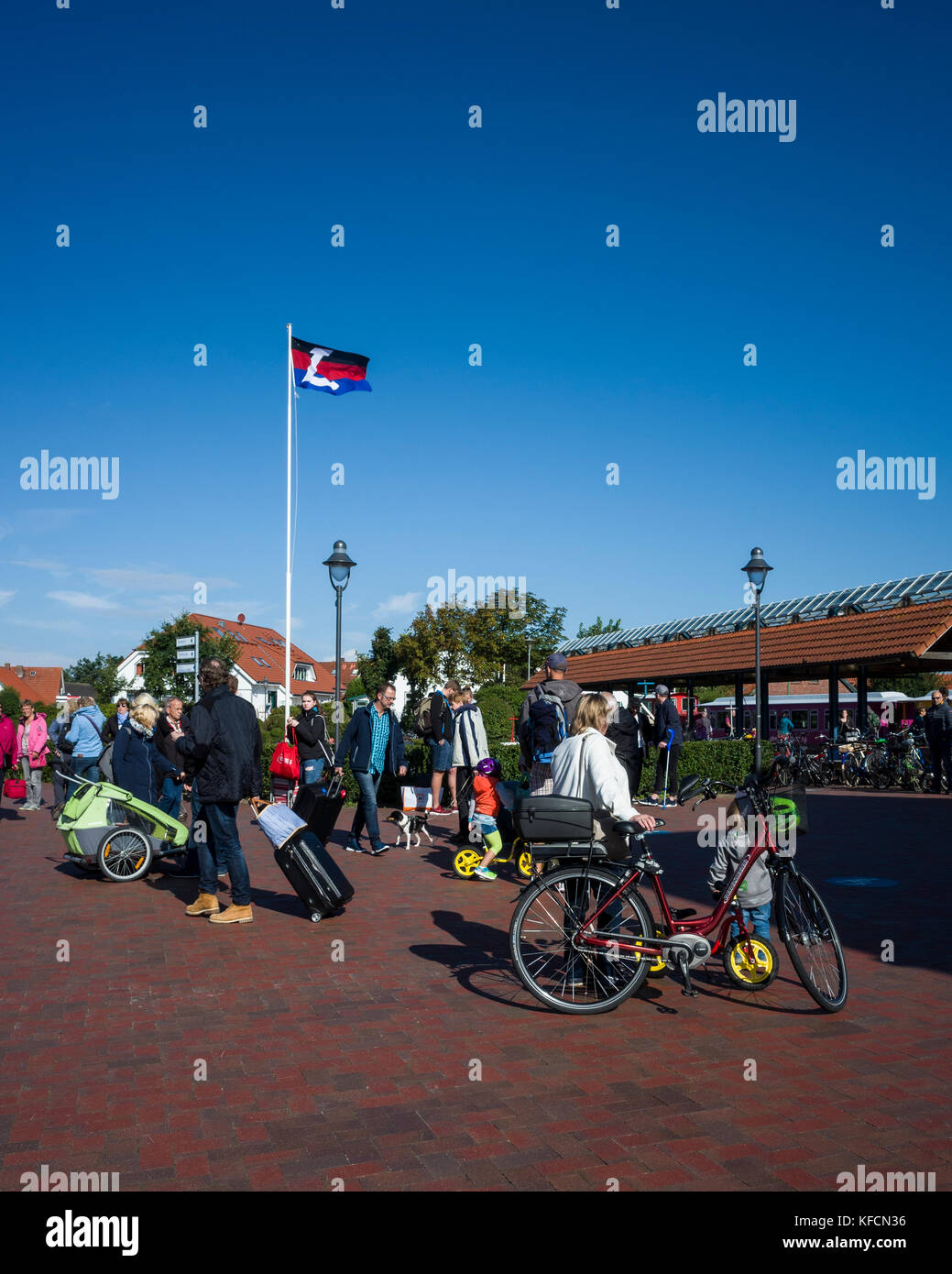 Inselbahnhof, Langeoog.  Deutschland.  Germany.  A view of holiday makers on the platform of the island's railway station.  The Langeoog flag flying high against the blue sky on a bright sunny day. Stock Photo