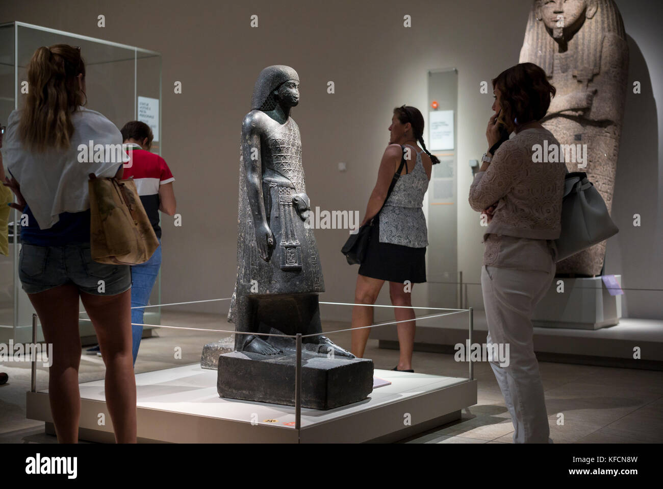 Turin. Italy. Visitors at the Museo Egizio (Egyptian Museum) looking at exhibits.  Pictured, egyptian statue of Aanen, second priest of Amon. New King Stock Photo