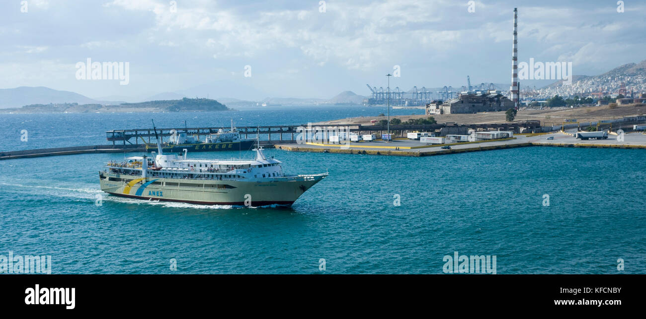 Port of Piraeus, Athens.  Greece.  A view across the water towards the docks on the other side of the harbour.   A ship is entering the port.  It's a bright overcast day. Stock Photo