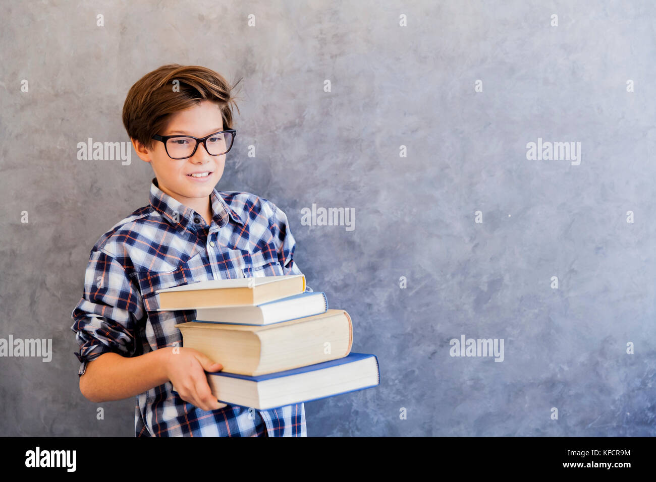 Cute teenage school boy holding books against wall Stock Photo - Alamy
