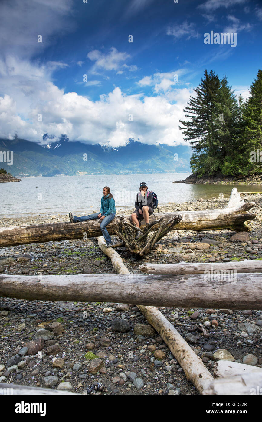 CANADA, Vancouver, British Columbia, Eric and Stepahnie Petersen sit atop drift logs at Brigade Bay on Gambier Island, in the Howe Sound with the Brit Stock Photo