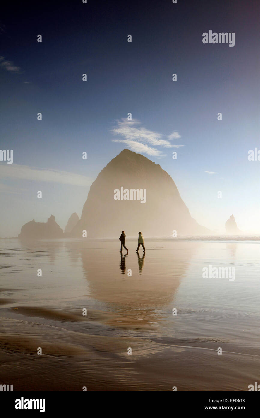 USA, Oregon, Pacific City, individuals walk along Pacific City Beach with Haystack Rock in the distance Stock Photo