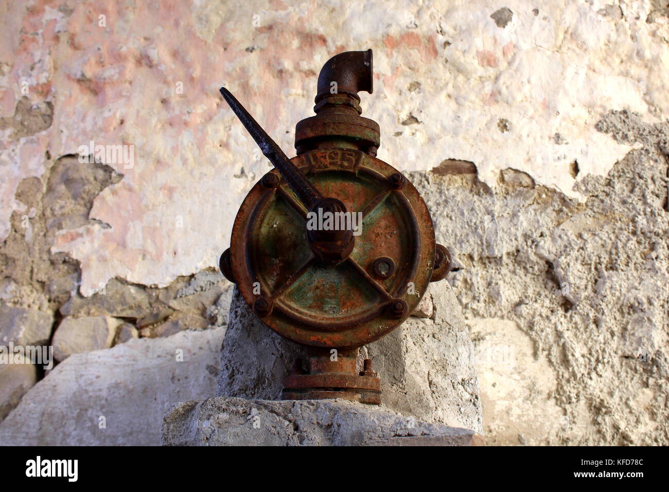 Old and completely rusted traditional water valve for hand pumps installed at town squares in front of stone wall Stock Photo