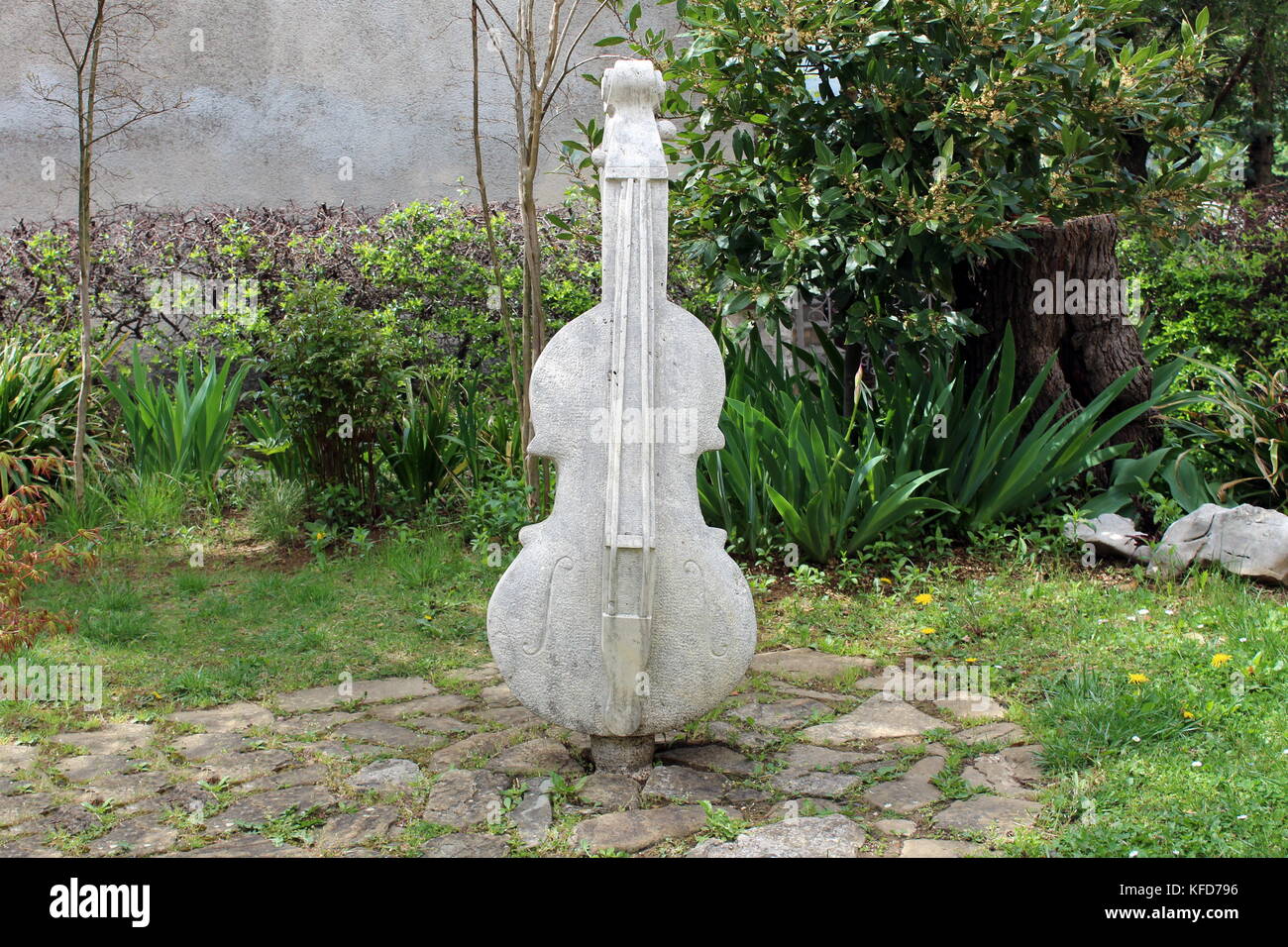 Double bass stone statue on stone tiles and surrounded with trees