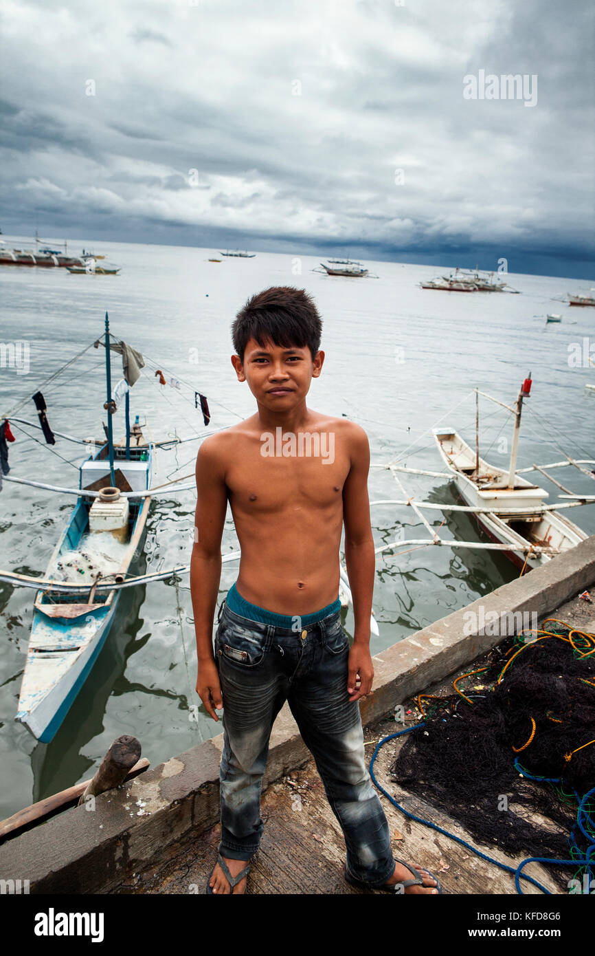 PHILIPPINES, Palawan, Puerto Princesa, young fisherman stands in front of fishing boats at Liberty Fishing Village Stock Photo
