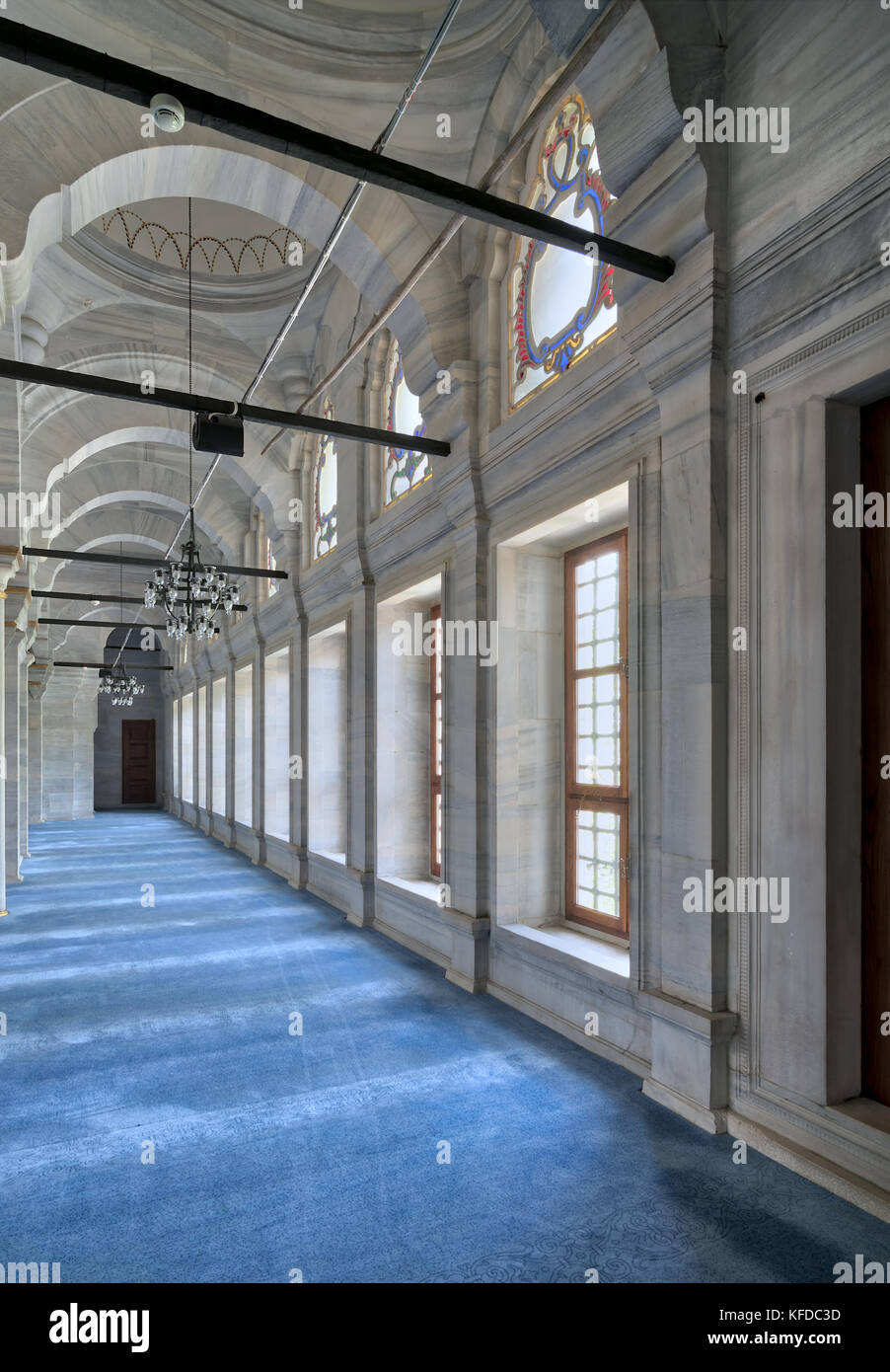 Passage in Nuruosmaniye Mosque, a public Ottoman Baroque style mosque, with columns, arches and floor covered with blue carpet lighted by side windows Stock Photo