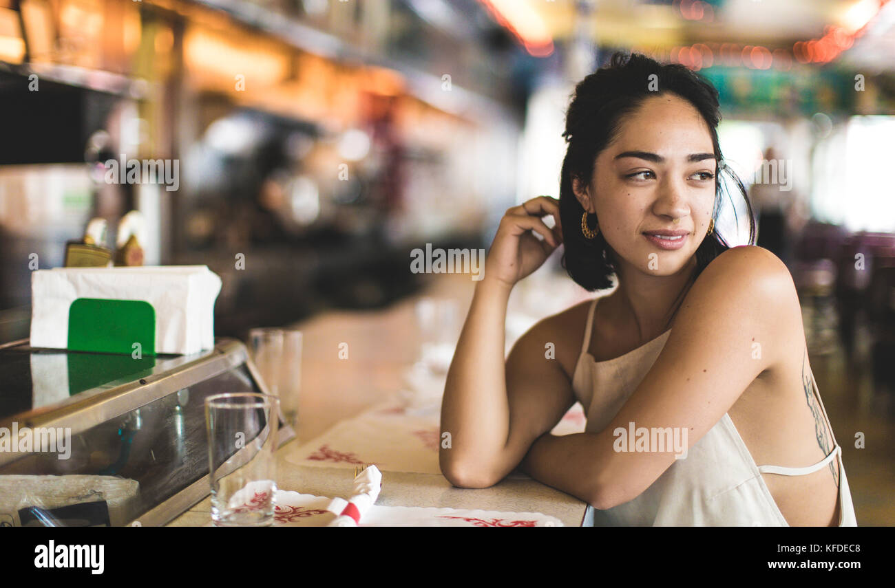 Young woman sitting at a bar counter looking over her shoulder, hand in her hair. Stock Photo