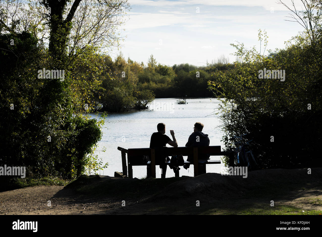 Two men sat by lake enjoying warm autumn sun Stock Photo