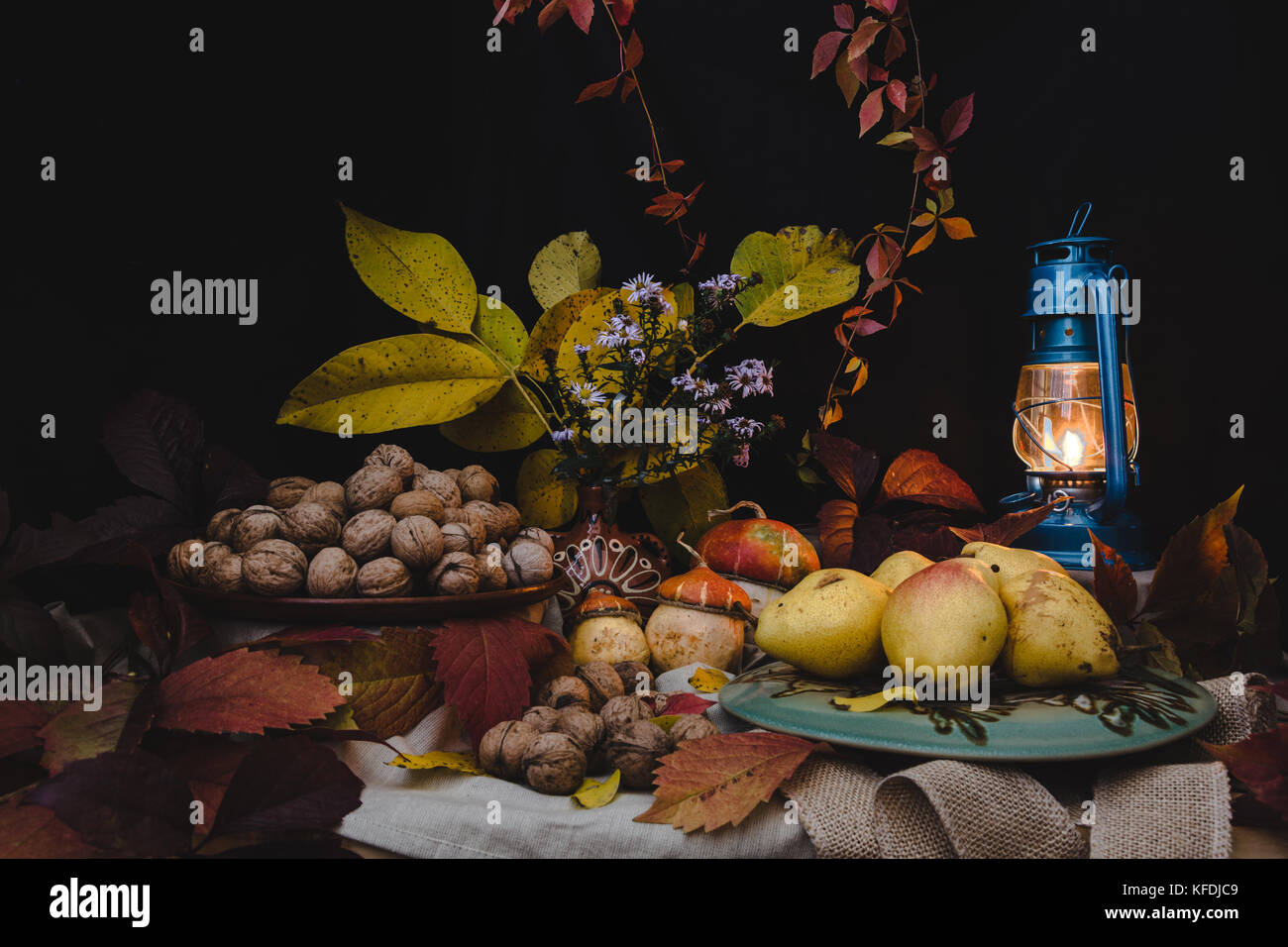 The autumn still life is decorated with a pear, walnut, pumpkin, autumn leaves and a kerosene lamp Stock Photo