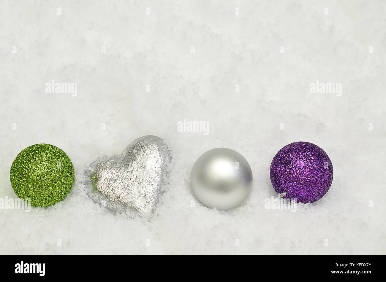 close up of silver, green and purple Christmas tree decorations on snow background Stock Photo