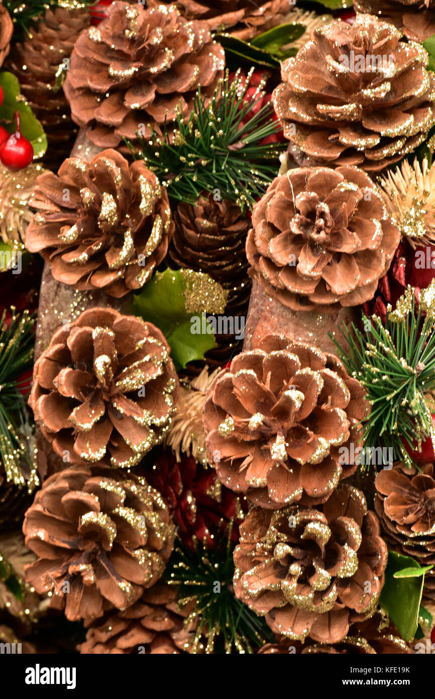Fir cones and pine cones, tinsel and holly with berries in red as decorations on a christmas tree for the festive season. Seasonal greetings. Stock Photo