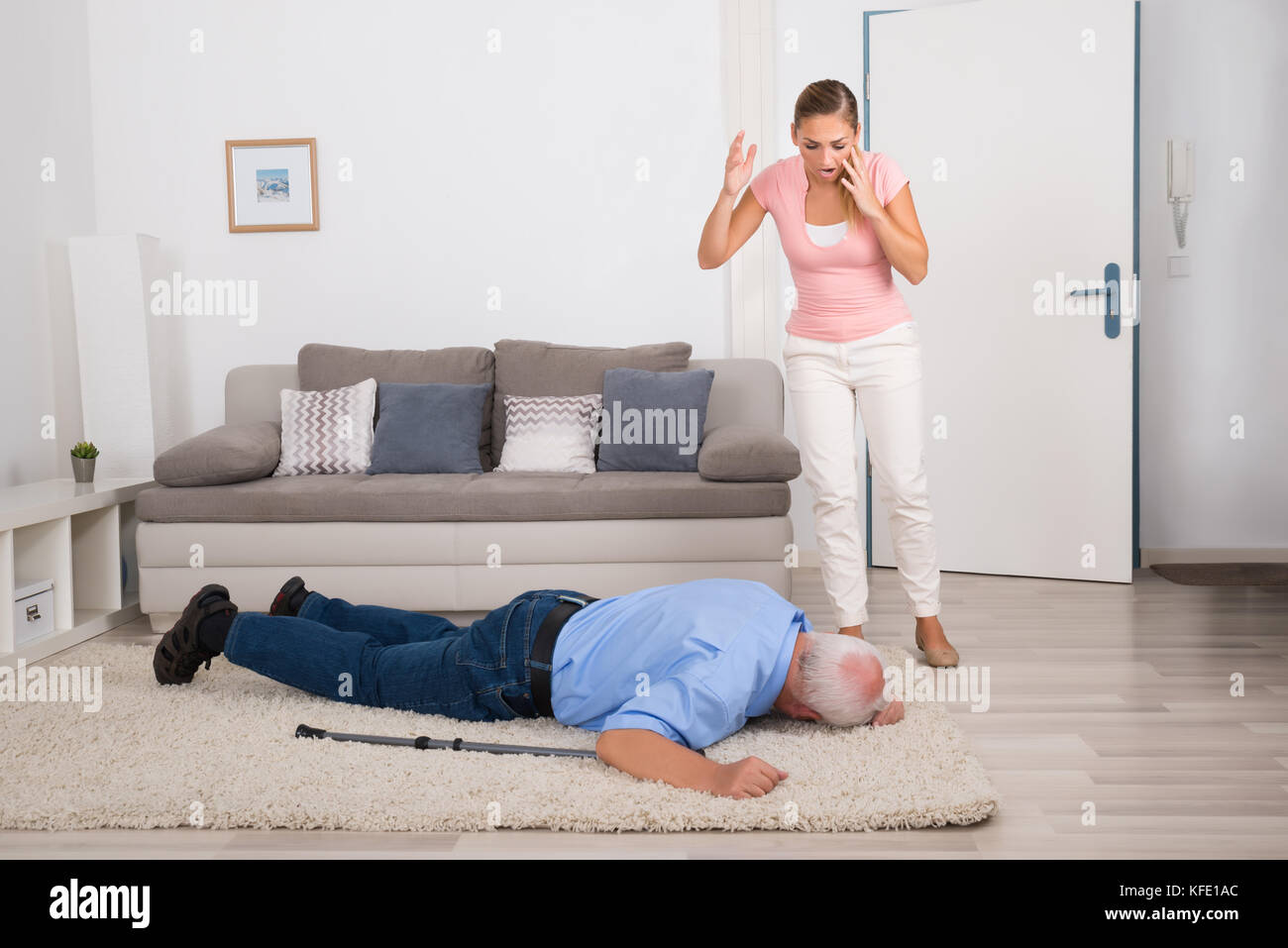 Shocked Young Woman Looking At Her Fainted Disabled Father Lying On Carpet Stock Photo