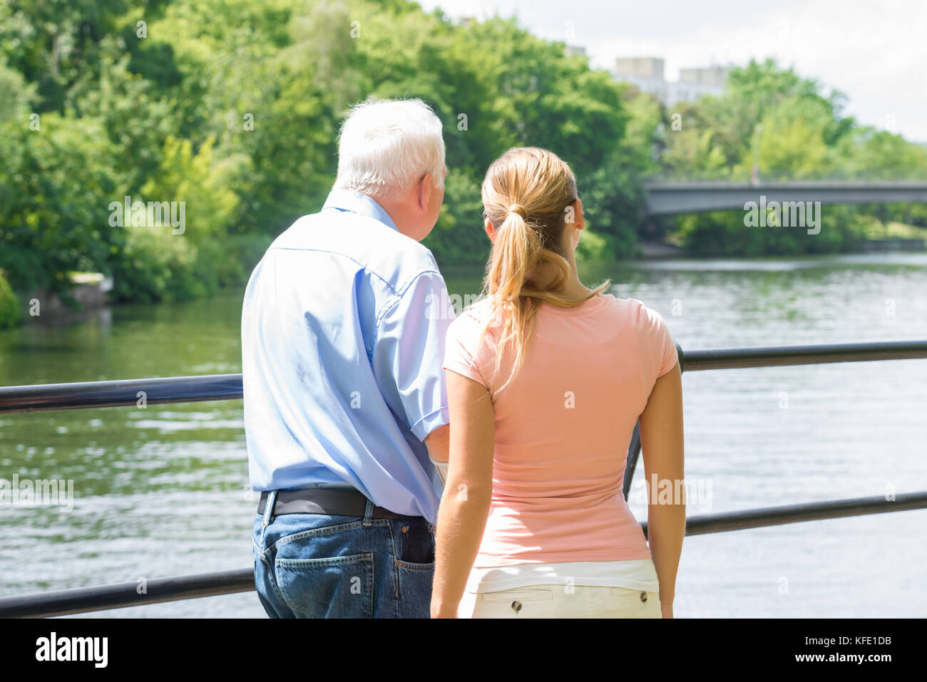 Rear View Of A Young Woman With Her Father Looking At Lake Stock Photo