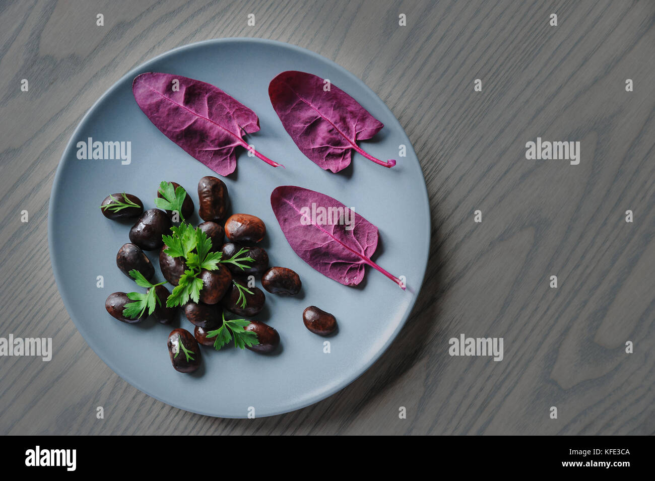 Plate with dark  beans and red spinach leaves placed on wooden table top. Stock Photo