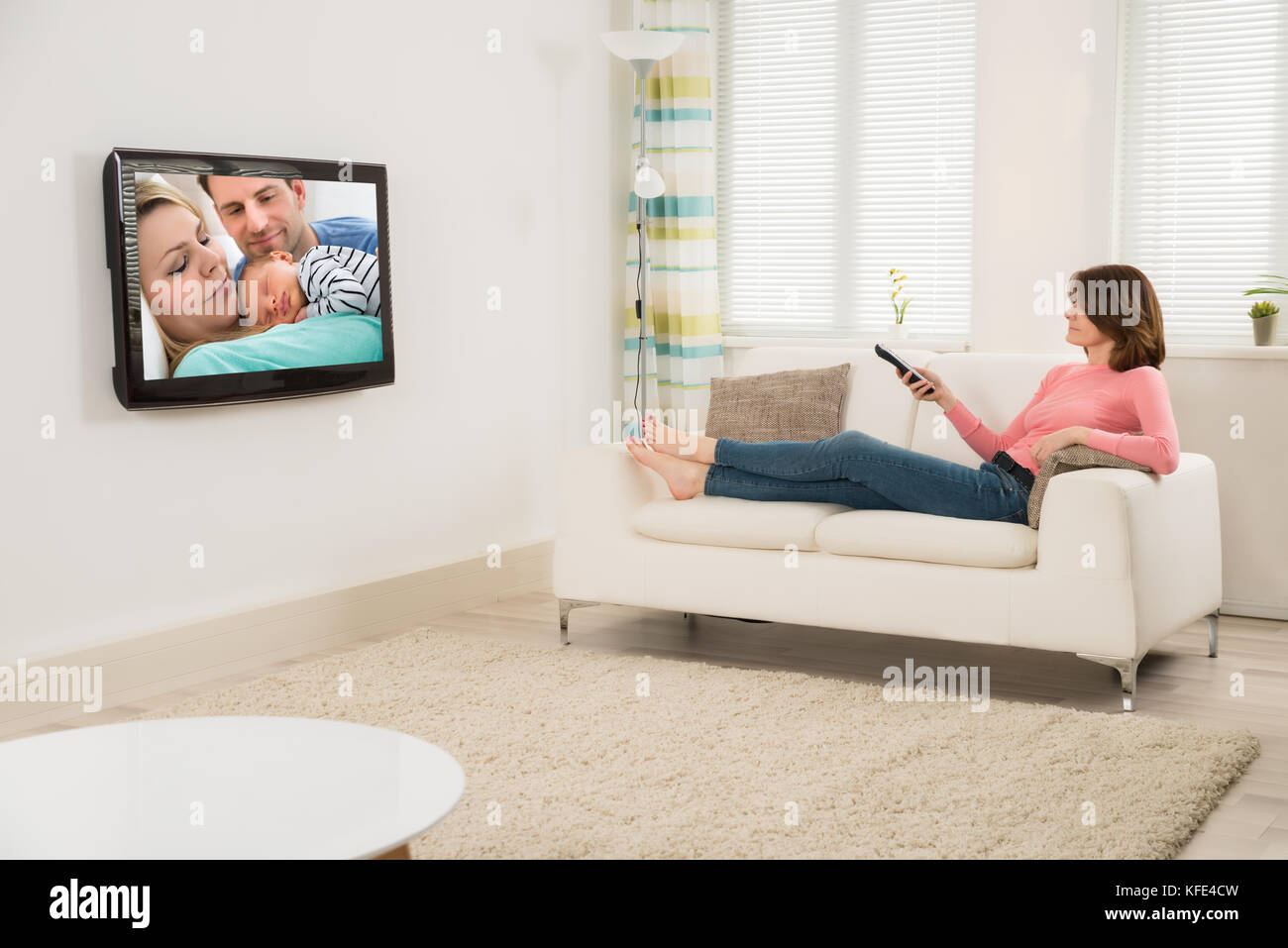 Young Woman Watching Television While Lying On Sofa At Home Stock Photo