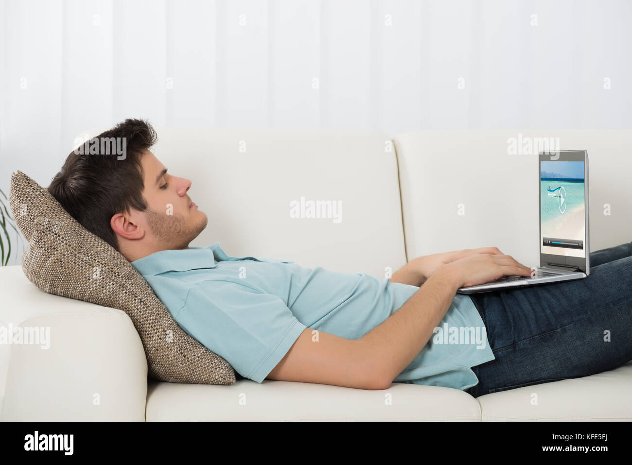 Young Man Lying On Sofa Watching Video On Laptop Stock Photo