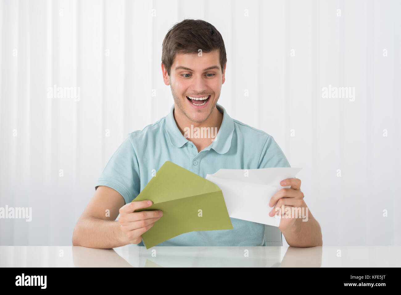 Happy Man Holding Letter With Green Envelope On Desk Stock Photo