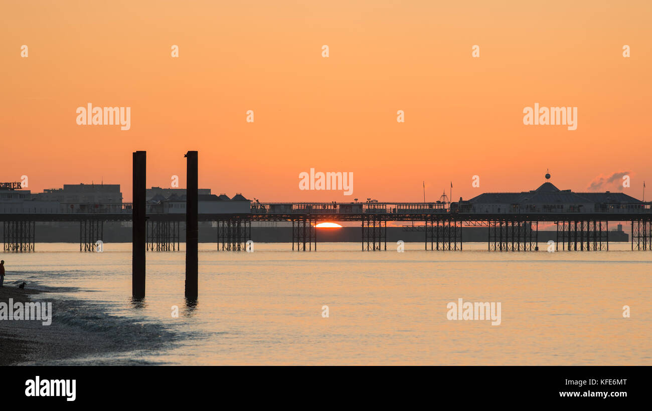 A man With a Dog Watches the Sun Appear on the Horizon Behind the Palace Pier, Brighton, UK Stock Photo