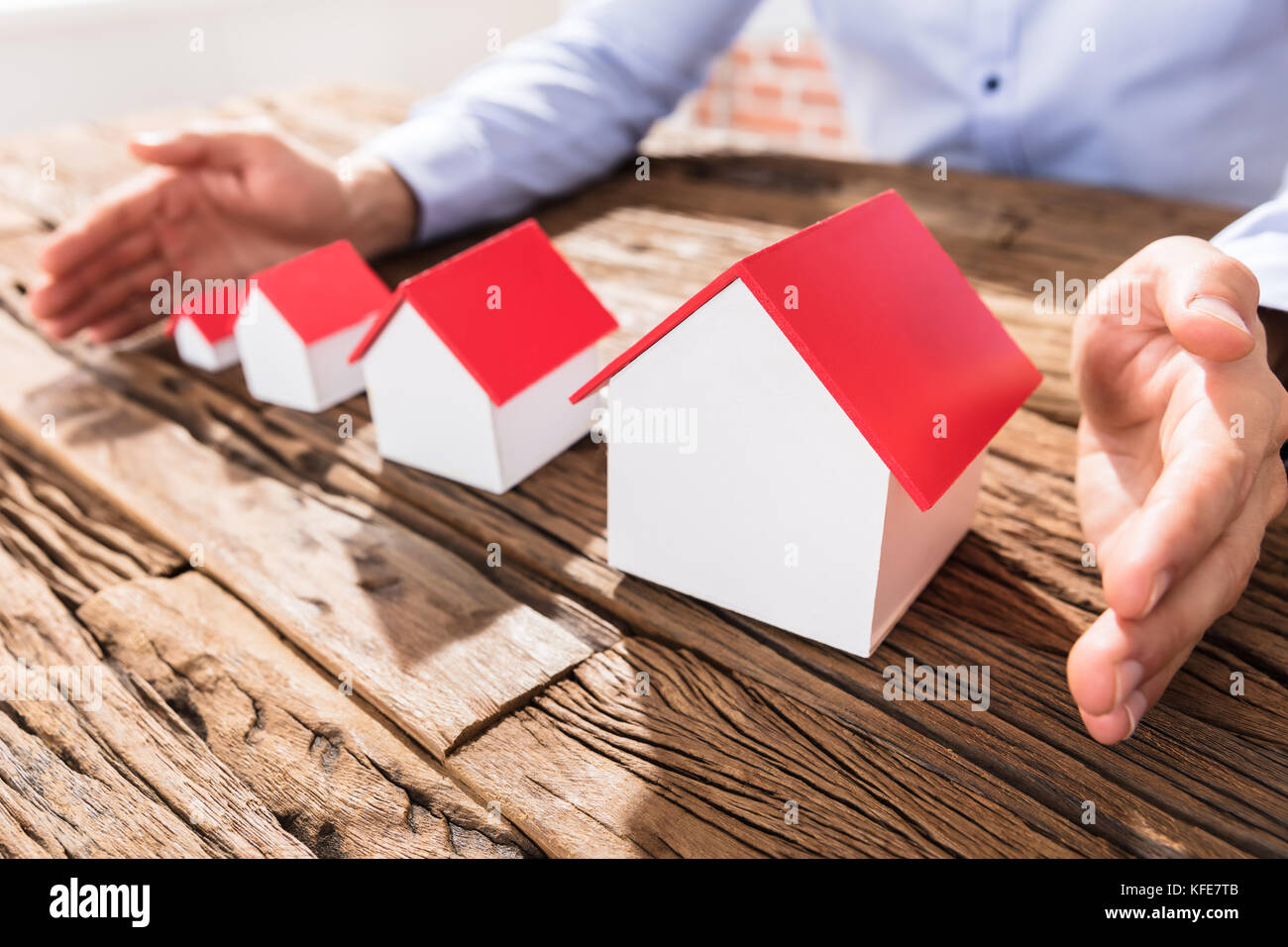 Close-up Of A Businessman Protecting The Scales Of House Models With Hands Stock Photo