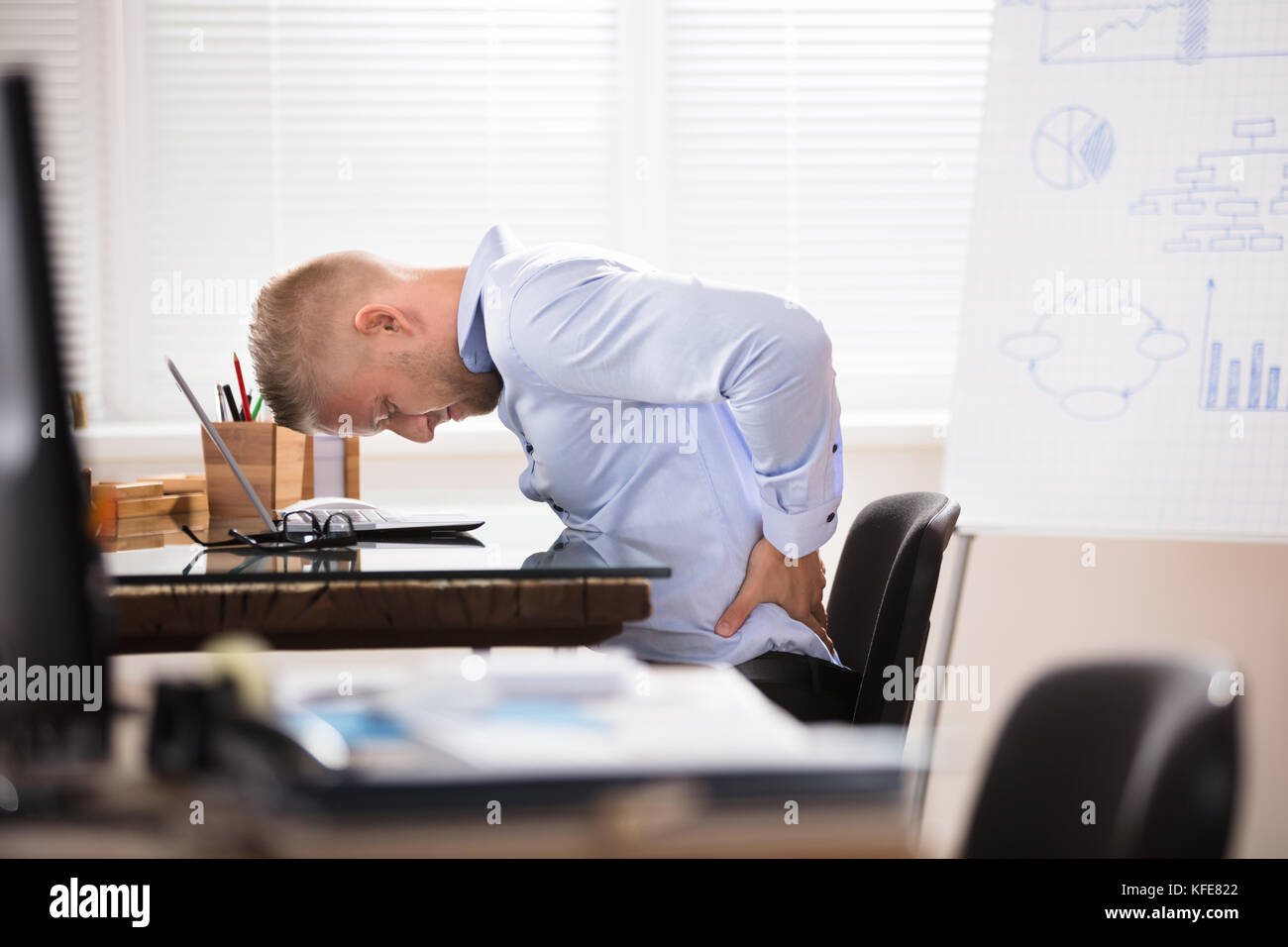 Businessman Sitting At Desk With Laptop Having Back Pain In Office