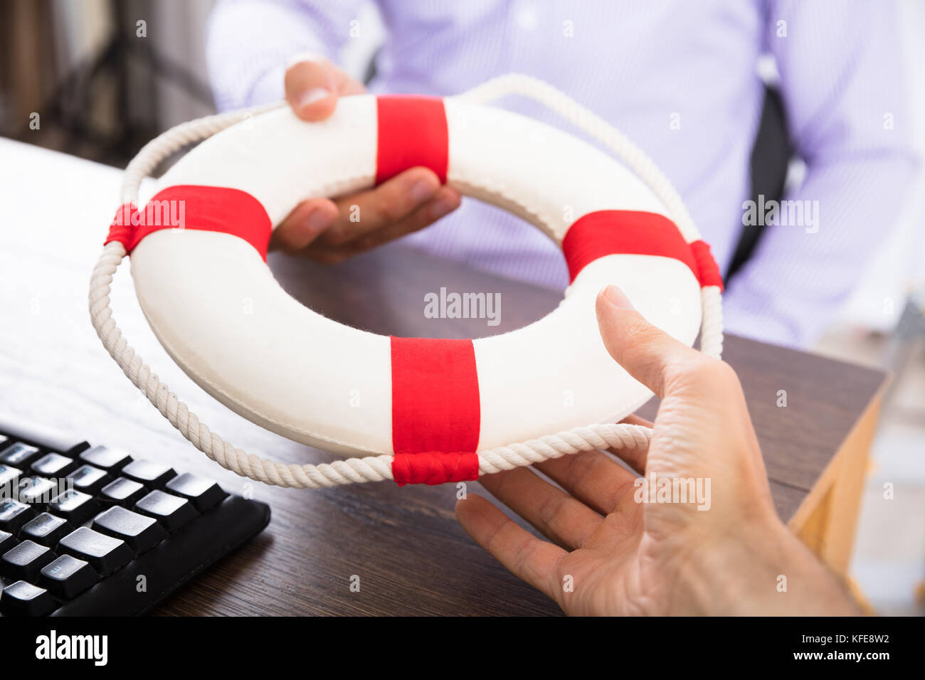 Close-up Of A Businessman's Hand Passing A Lifebuoy To His Partner In The Office Stock Photo