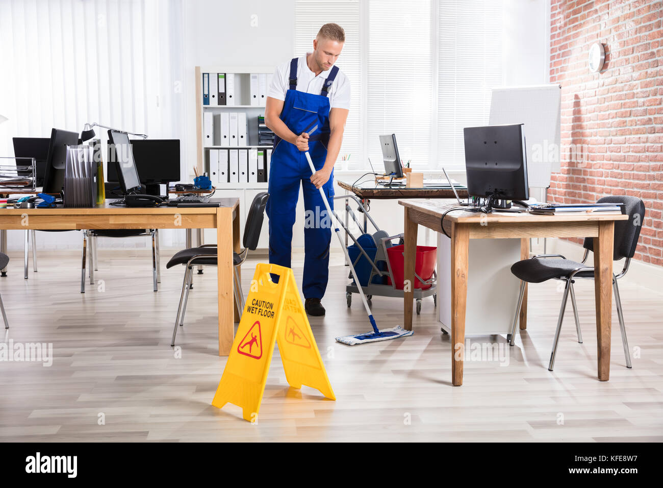 Male Janitor Cleaning Floor With Caution Wet Floor Sign In Office Stock ...