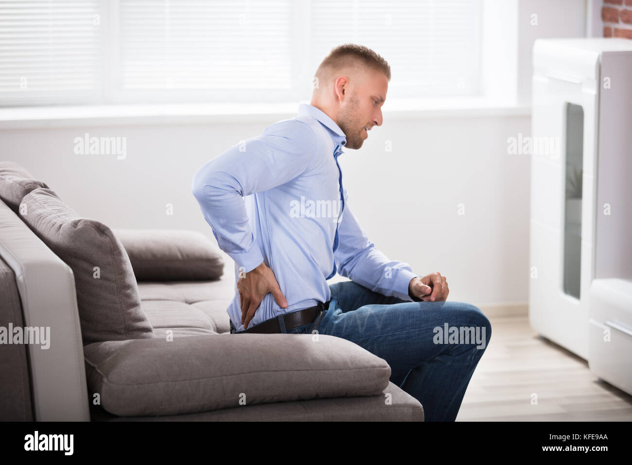 Man Sitting On Sofa Suffering From Back Pain At Home Stock Photo