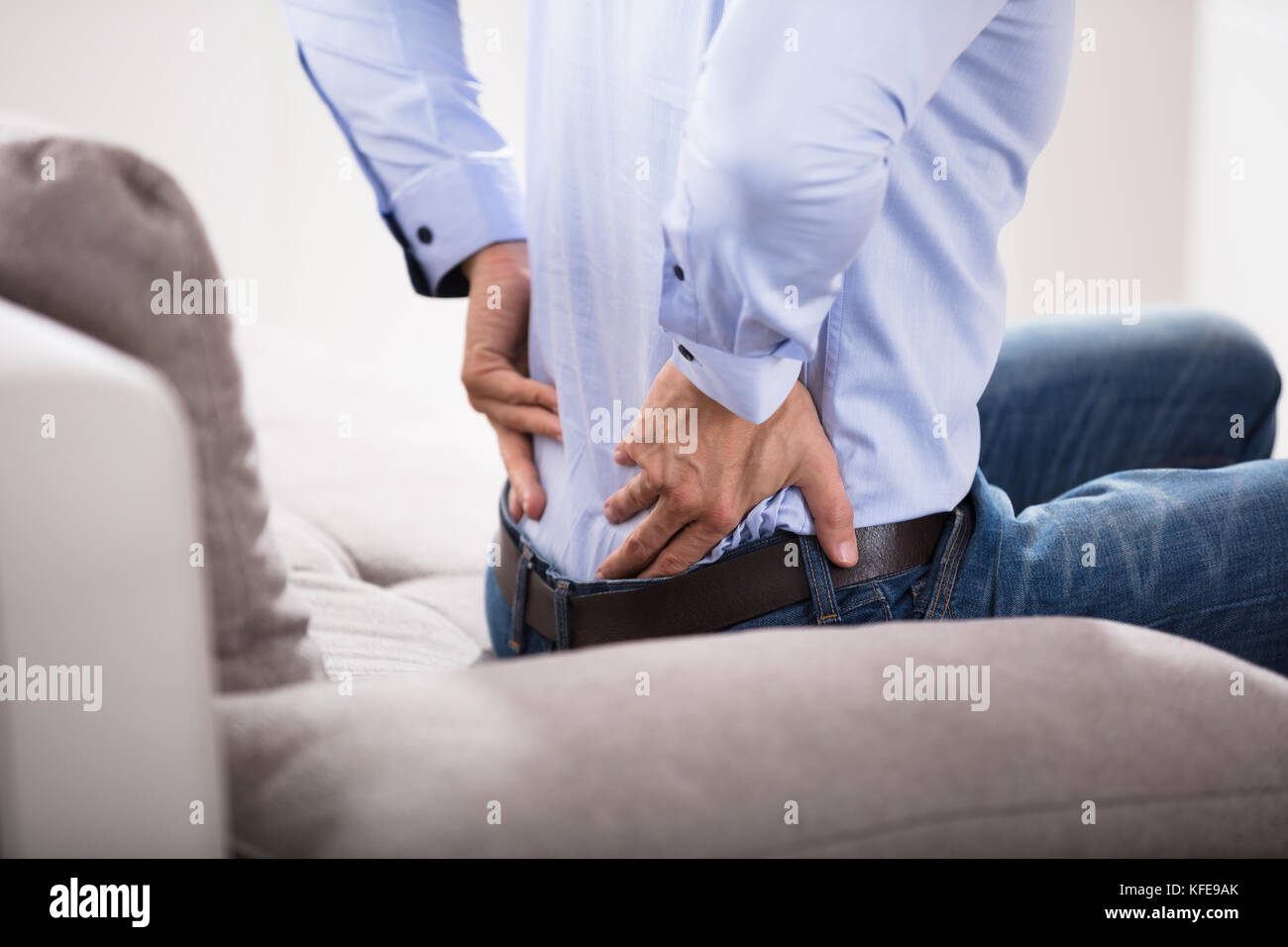 Close-up Of A Person Sitting On Sofa Suffering From Backache At Home Stock Photo
