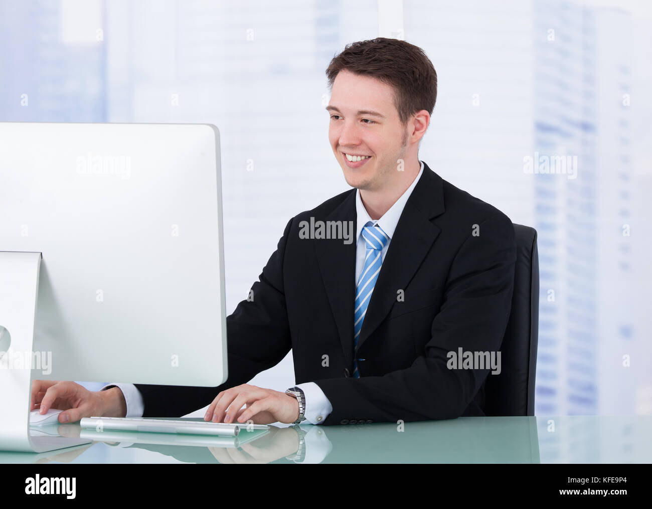 Portrait of confident young businessman using computer at office desk ...