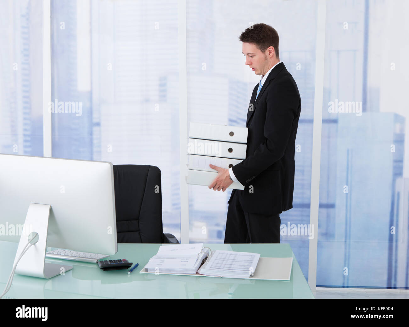 Side view of young businessman carrying stacked binders at office desk