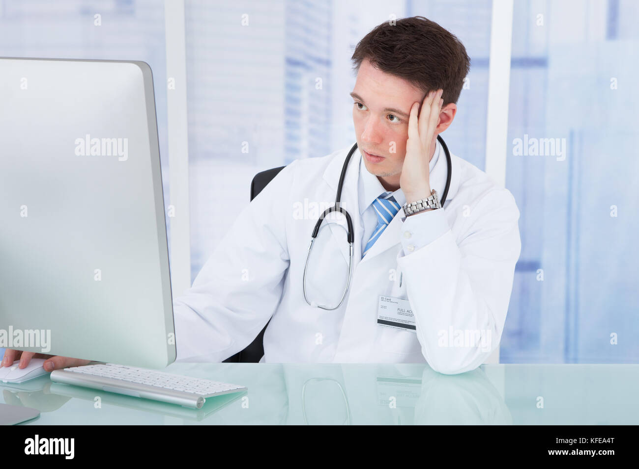 Worried young male doctor using computer at desk in hospital Stock Photo