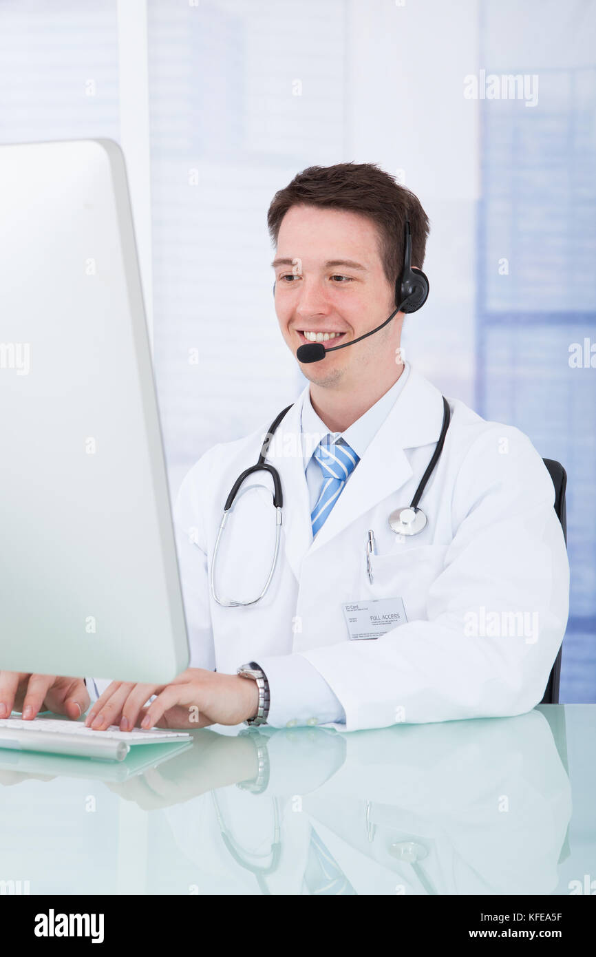 Portrait of young male doctor wearing headset while using computer at ...