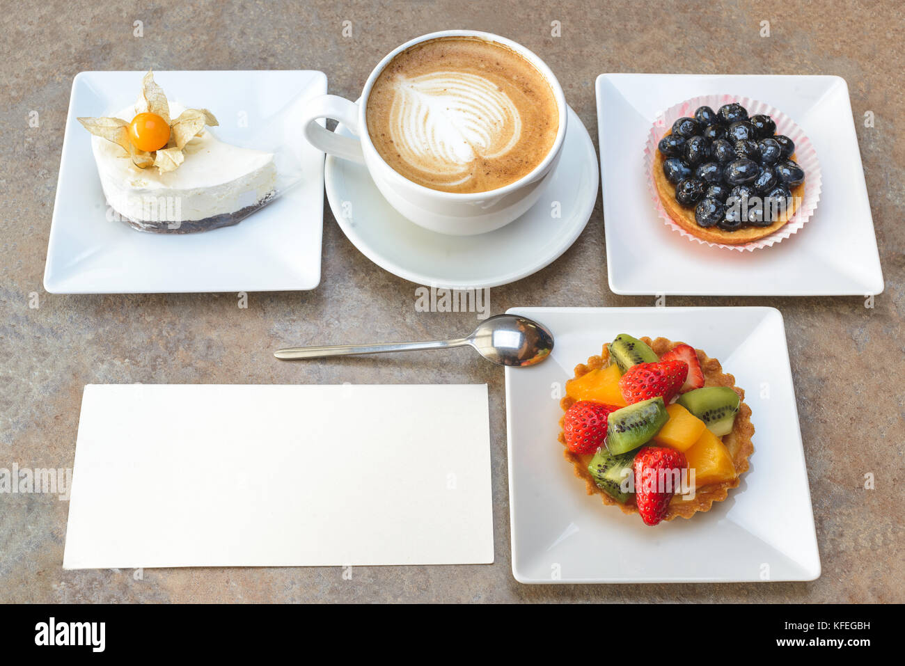 Different fruit cakes and cup of capuccino with blank card on table Stock Photo
