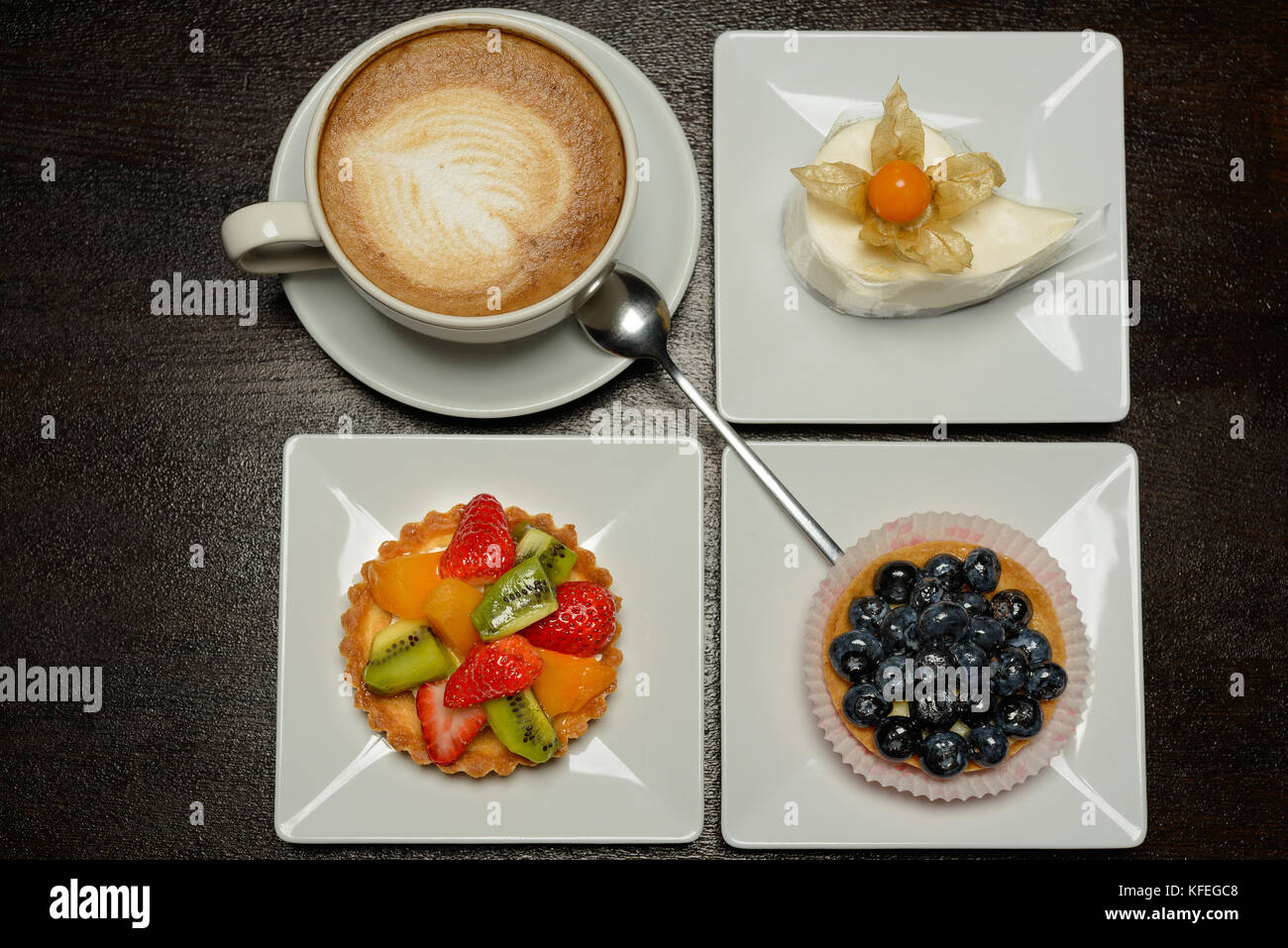 Different fruit cakes and cup of capuccino with blank card on table Stock Photo