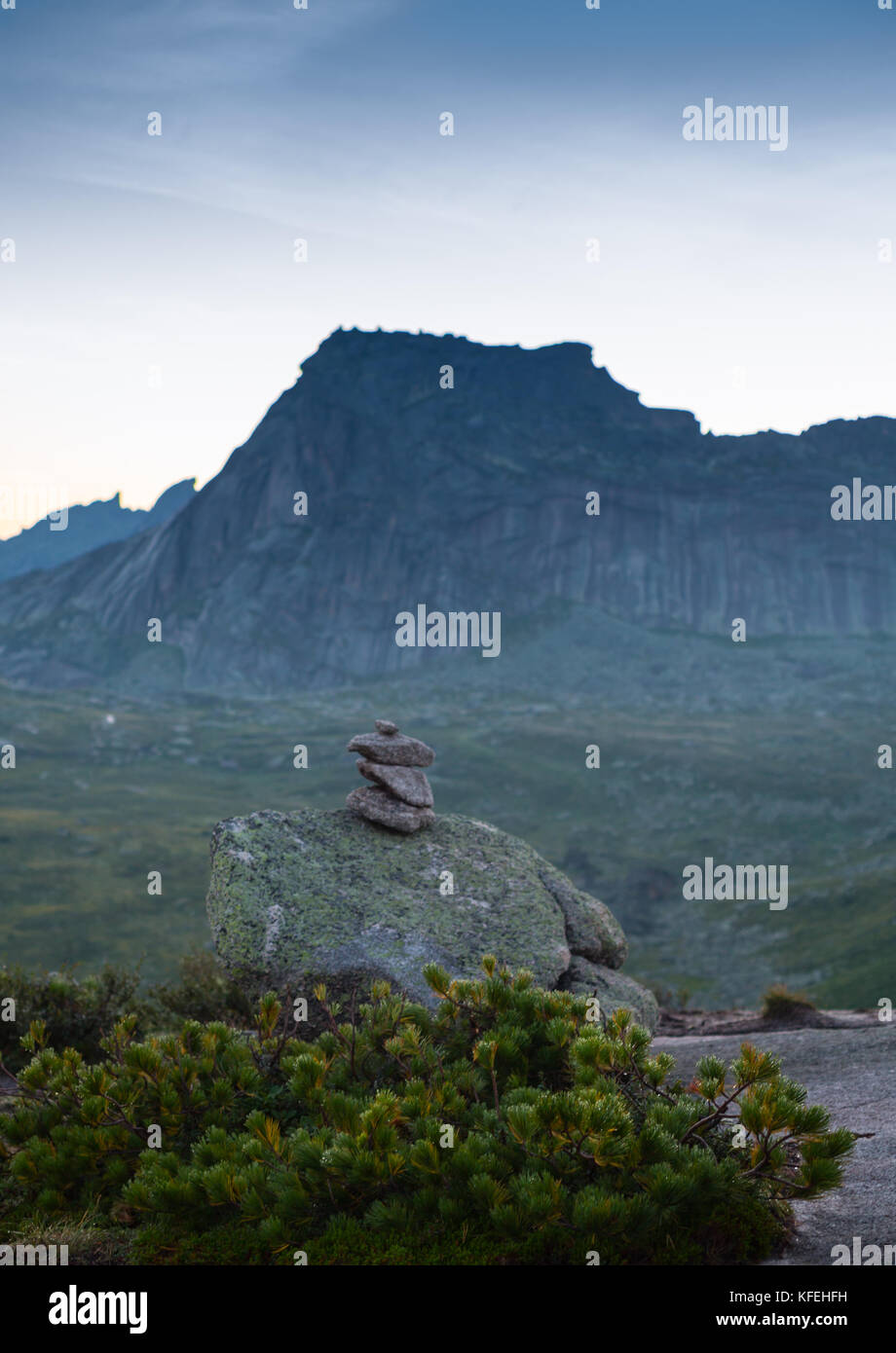Hanging stone lies on sloping surface of mountain above precipice. A huge boulder of granite and syenite is supported by a small area on mountain. Ergaki Park. Russia Stock Photo
