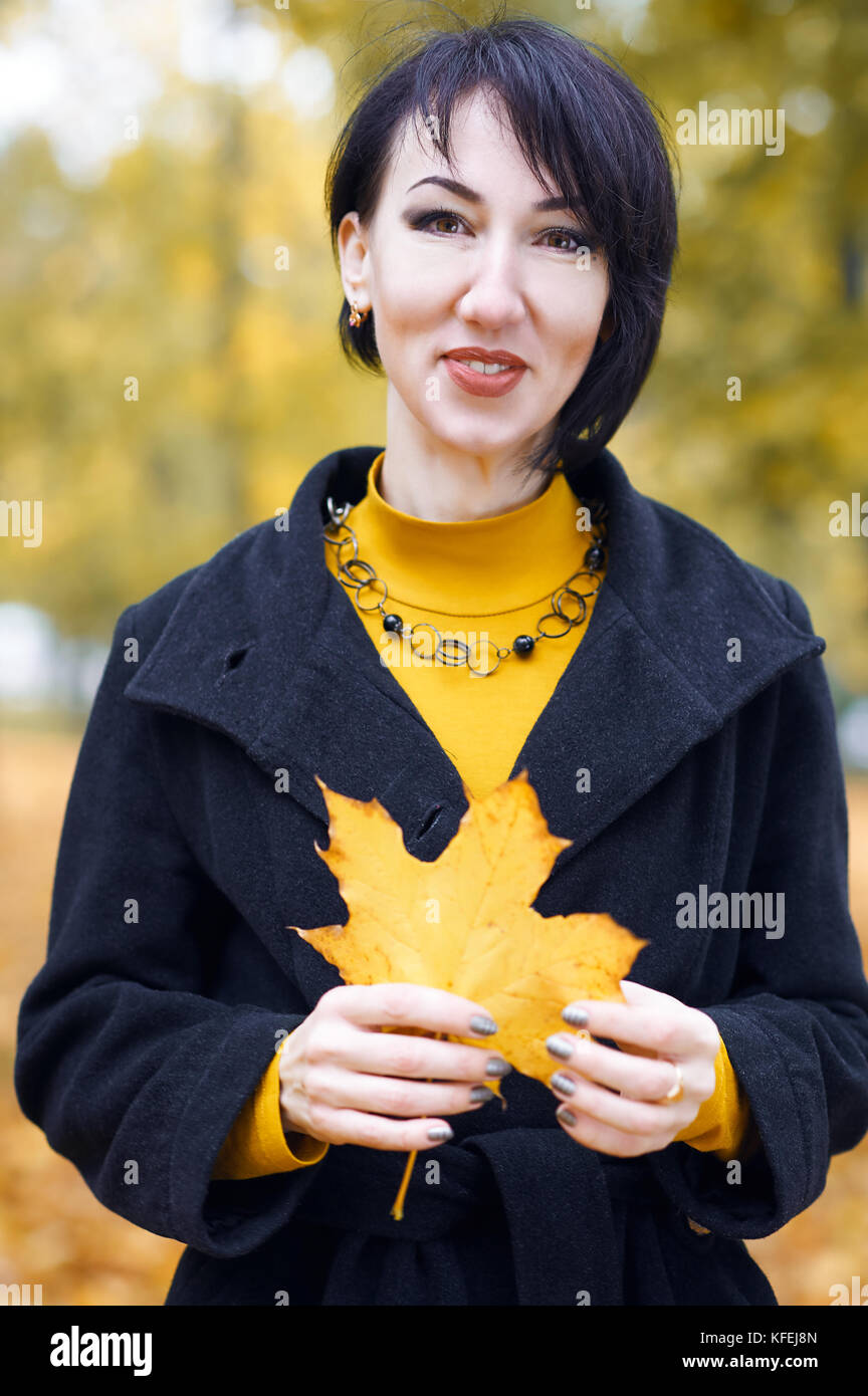 beautiful girl portrait with yellow leaf in hand, autumn city park on ...