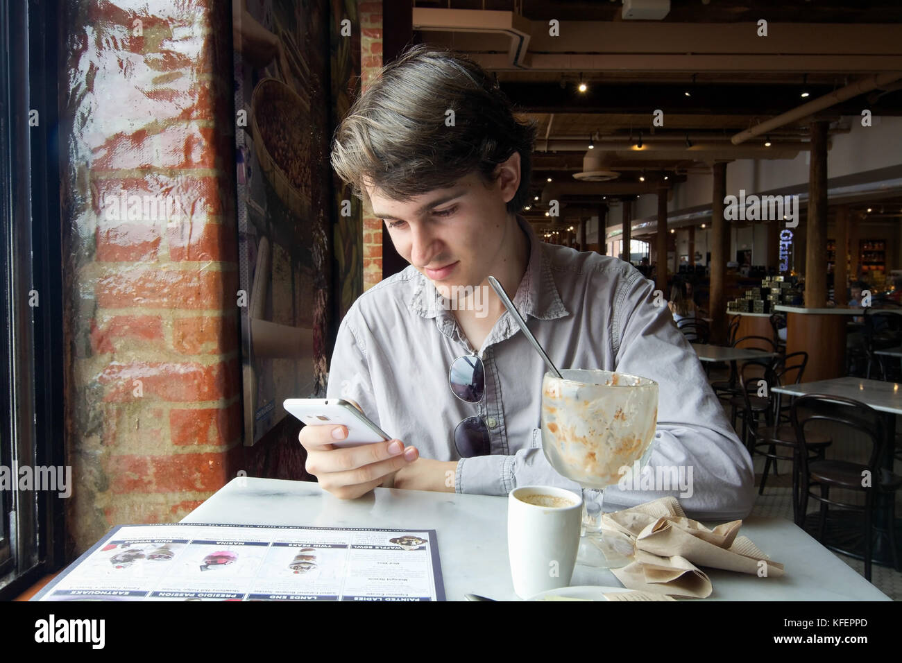 San Francisco, California, USA, 08 September 2017. Candid shot of unidentified young man smiling and checking the phone after consuming a sundae at Gh Stock Photo