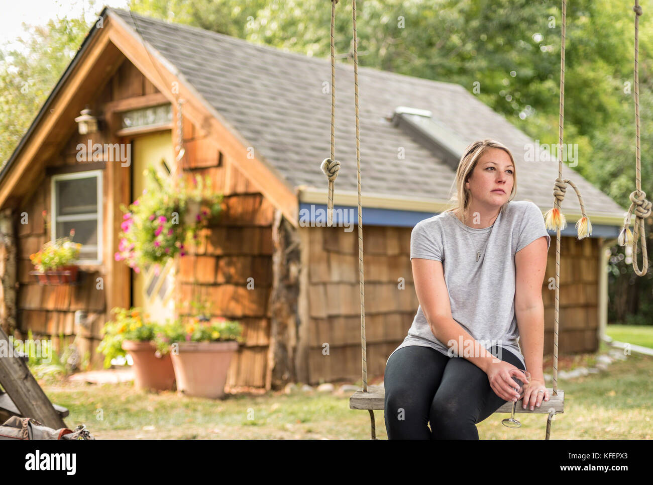millenial woman sitting in backyard on swing with glass of wine thinking Stock Photo