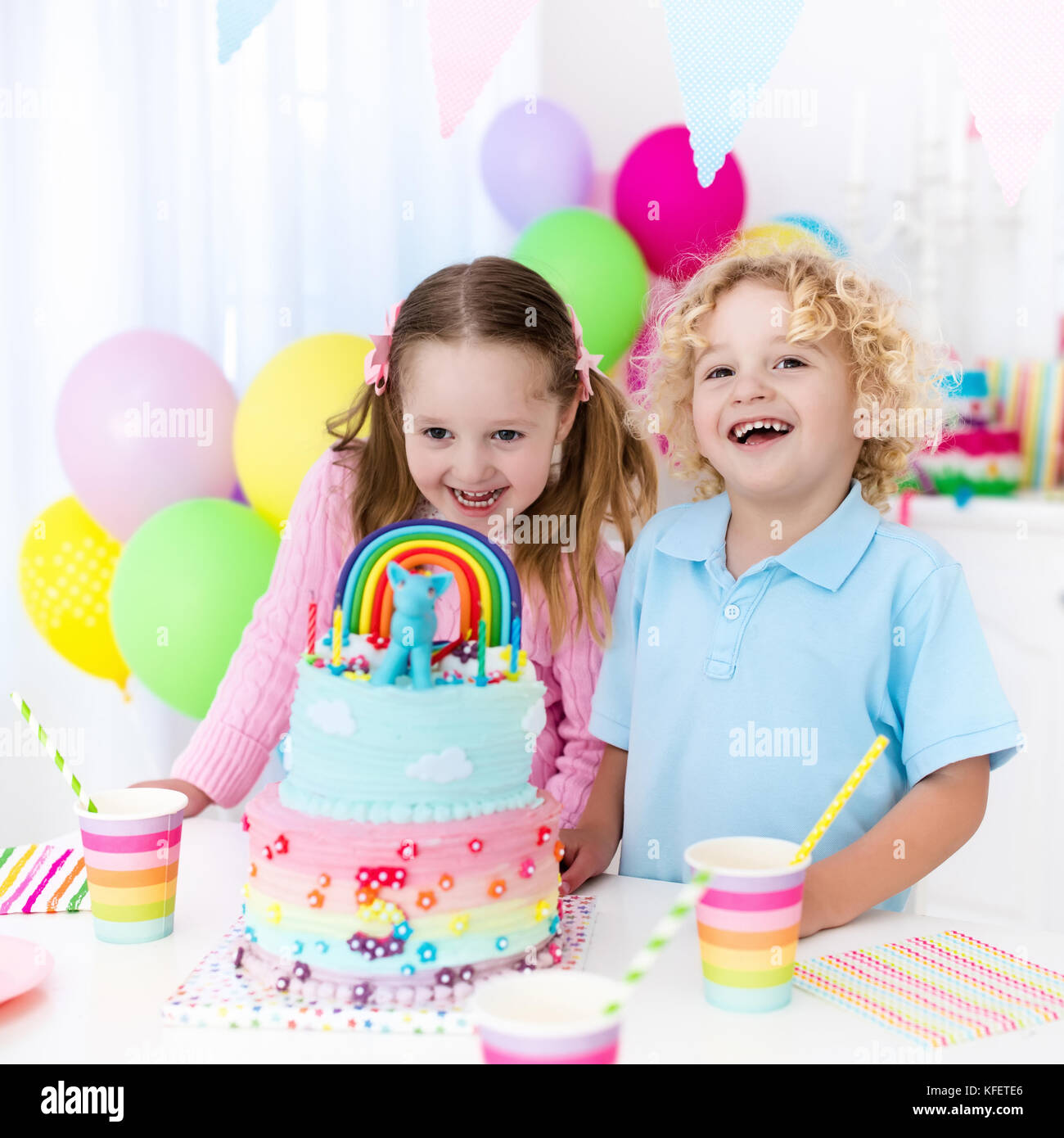 Kids birthday party with colorful pastel decoration and rainbow cake. Girl and boy with sweets, candy and fruit. Balloons and banner at festive decora Stock Photo