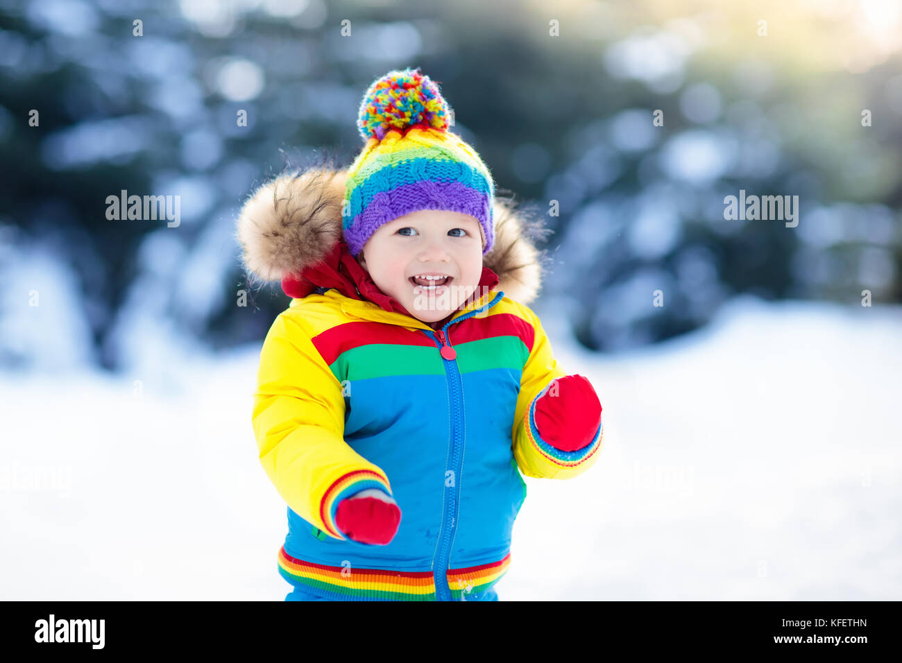 Child playing with snow in winter. Little boy in colorful jacket and ...