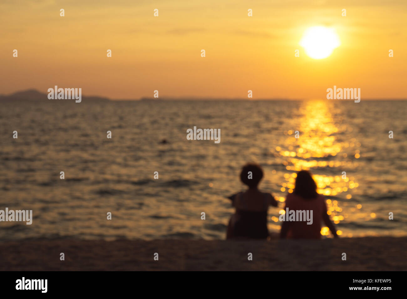 silhouette and blur of two middle-aged happy women sitting on the beach talking about old day and watching the sunset on the horizon. emotional and fr Stock Photo