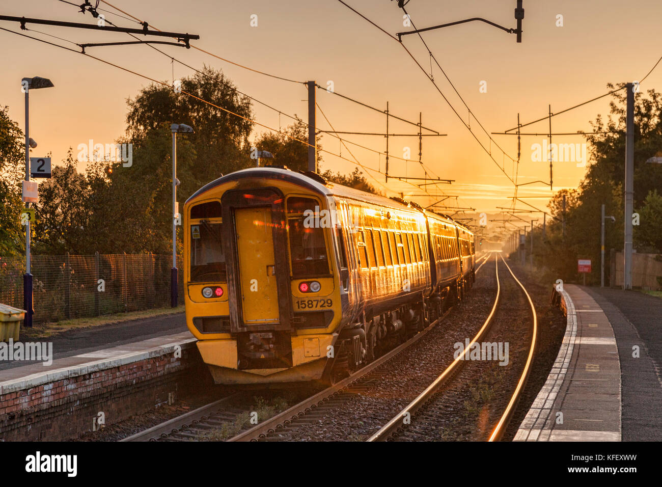 Early train leaving station with sun shining on it. Stock Photo