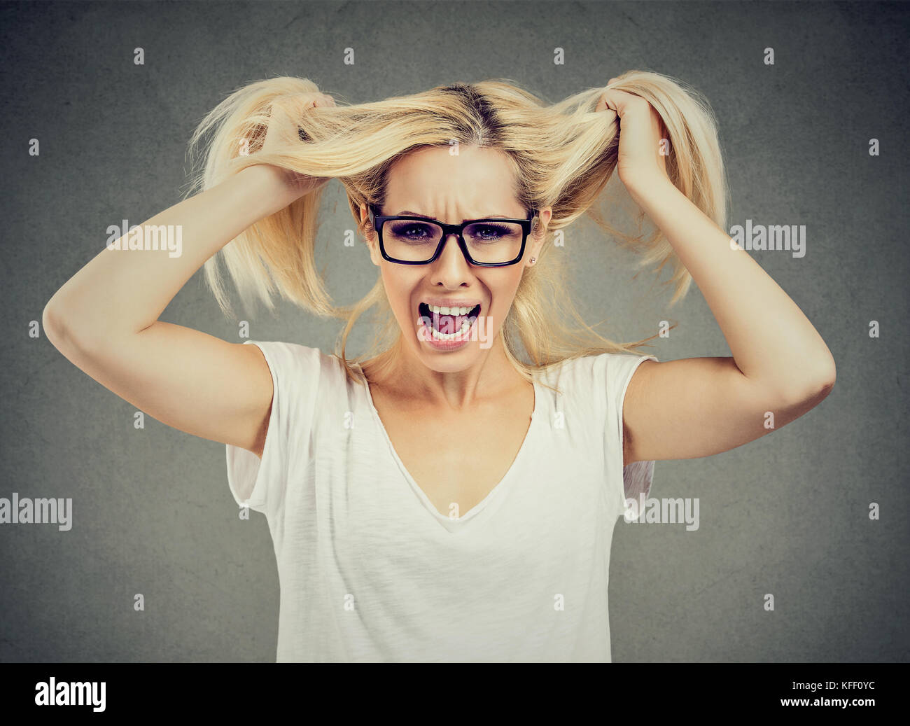 Angry woman screaming out loud and pulling her hair out isolated on gray background Stock Photo