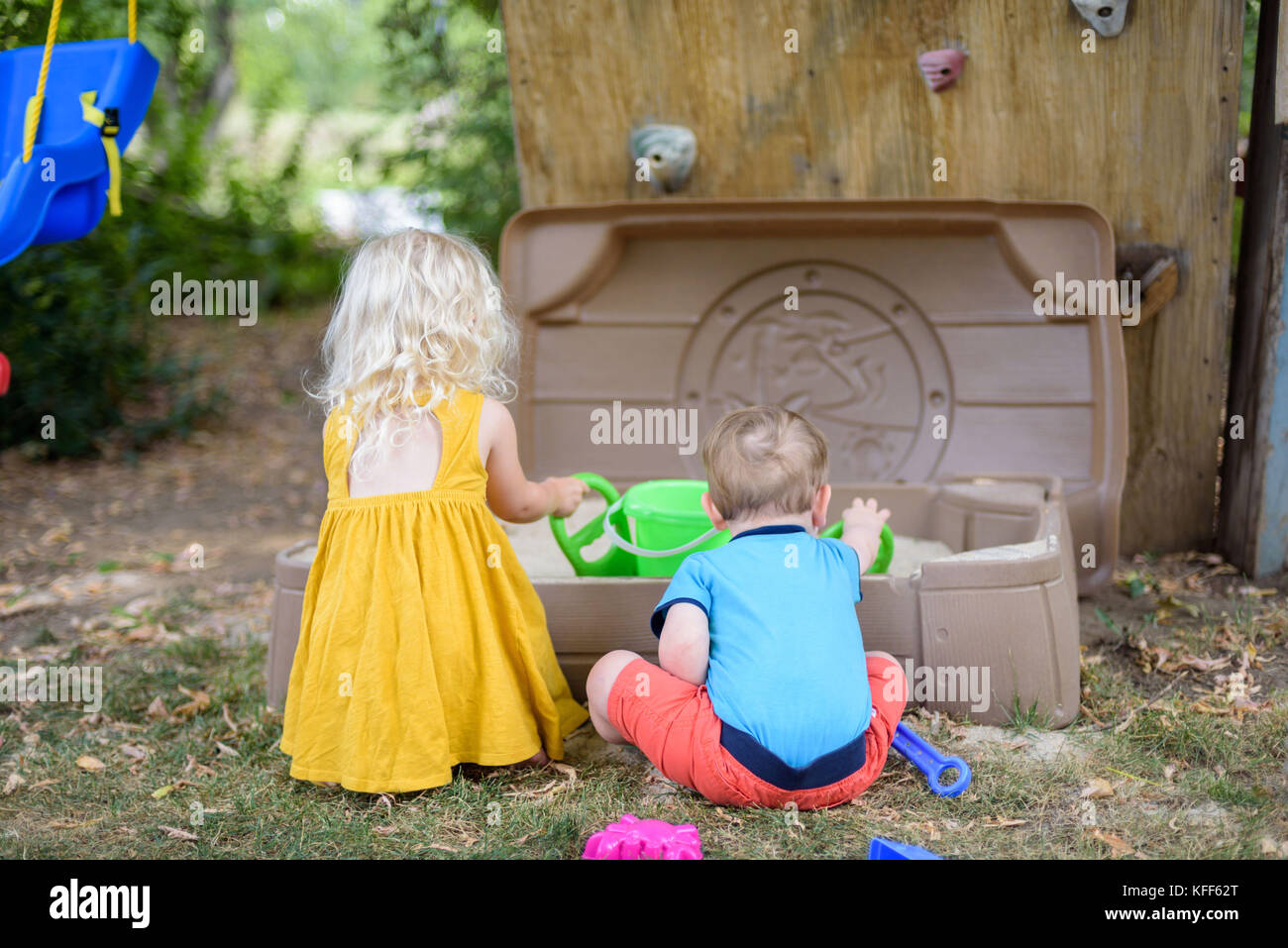 two small children playing in backyard sandbox in summer Stock Photo